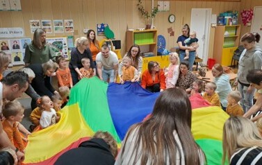 Dzieci z rodzicami uczestniczą w zabawię z chustą animacyjną 