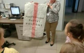 PRACOWNIK POCZTY PREZENTUJE KRASNOLUDKOM WOREK POCZTOWY.