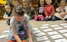 DZIEWCZYNKA PRZEKŁUWA PAPIEROWE SERCE , NA KT&Oacute;REGO ODWROCIE SĄ ZAPISANE MĘSKIE IMIONA.