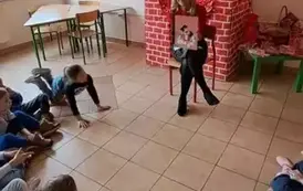 Dzieci siedzą i słuchają pani bibliotekarki, kt&oacute;ra czyta książkę 