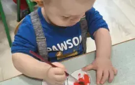 PRZEDSZKOLAK WYKONUJE PRACĘ PLASTYCZNĄ-MALUJE FARBAMI