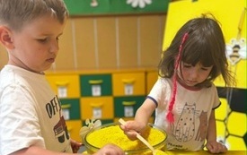 DZIECI ZA POMOCĄ ŁYŻECZEK PRZESYPUJĄ BARWIONY RYŻ DO "PLASTR&Oacute;W MIODU"