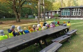 DZIECI SIEDZĄ NA ŁAWKACH PRZED BUDYNKIEM OŚRODKA EDUKACJI EKOLOGICZNEJ
