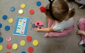 Dzień Kropki w grupie biedronek. Dziewczynka siedzi na dywanie obok niech są kropki i napis "Dzień Kropki"