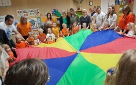 Dzieci z rodzicami uczestniczą w zabawię z chustą animacyjną 